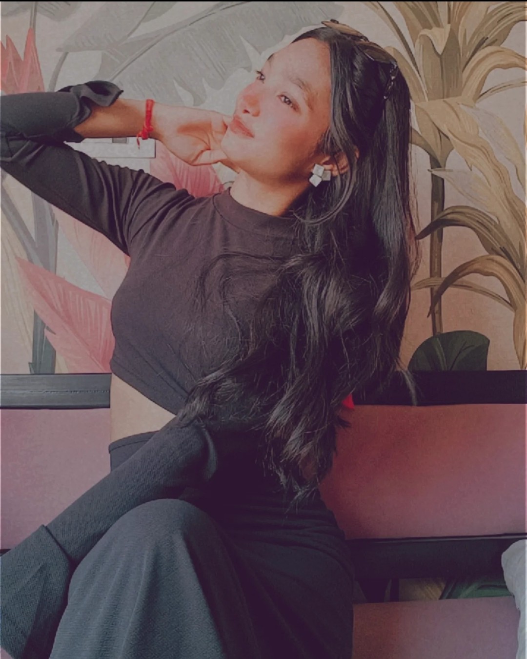 Tanya in a black crop top and pants, seated gracefully against a tropical mural